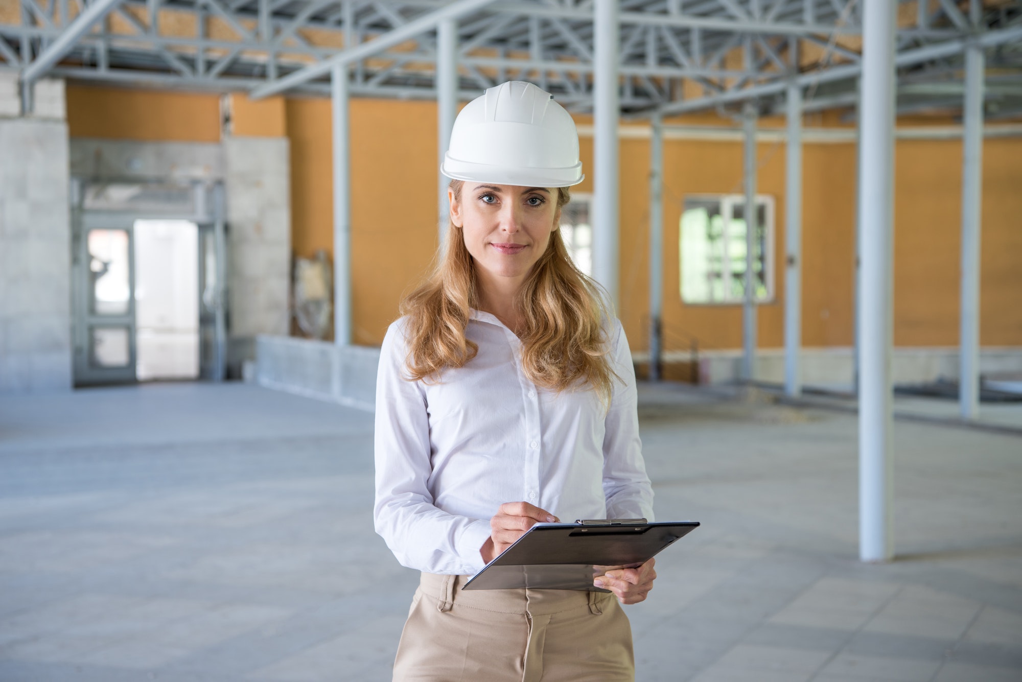 mature contractor in helmet making notes at clipboard and looking at camera